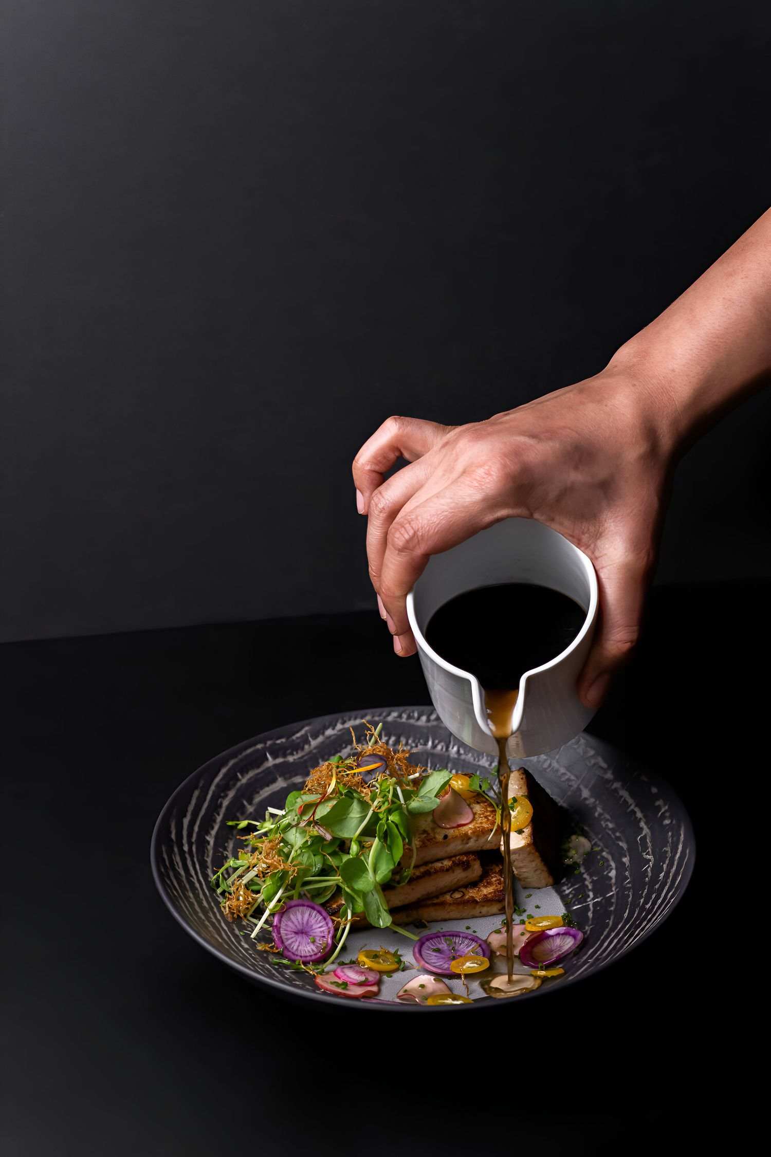 À la passe, le jus versé au pichet sur une assiette de la mise en bouche, fond noir