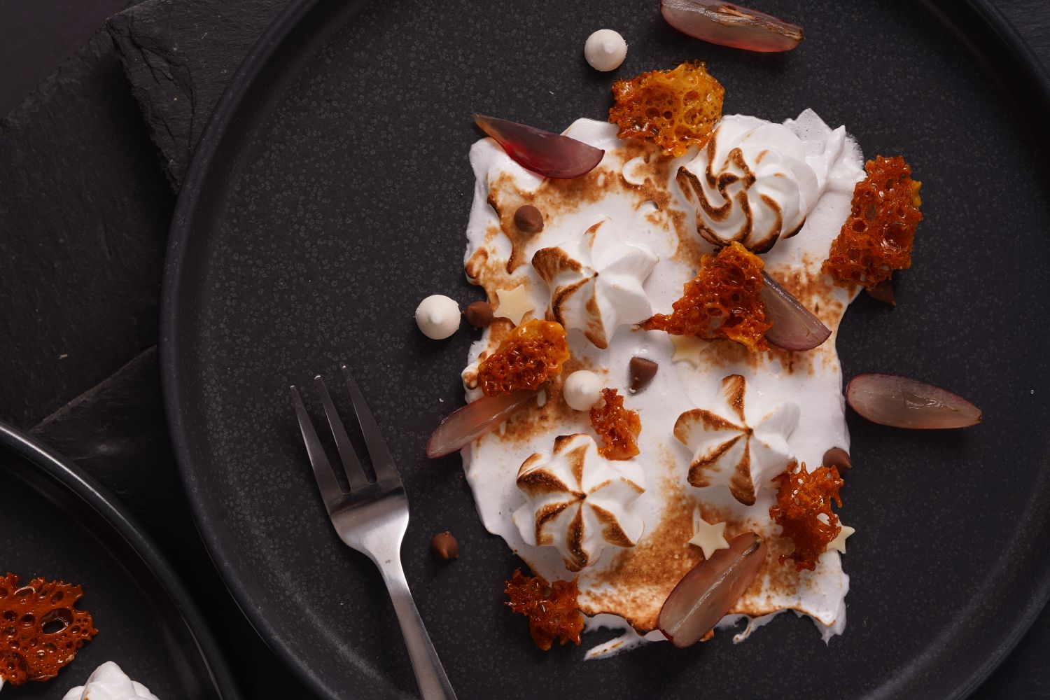 Meringue passée à la flamme, caramel en éclats dorés sur assiette sombre