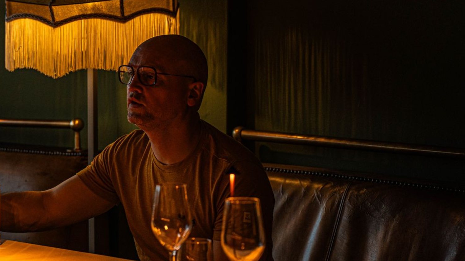 Un convive attardé sous la lampe à franges, verres de vin et banquette de cuir, la salle en fin de service
